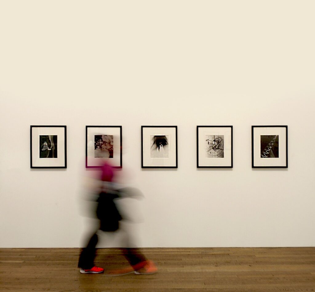 A blurry figure walking past five portraits on a wall. 