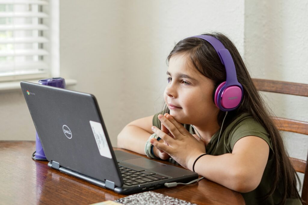 A young girl wearing pink headphones looking into her laptop.