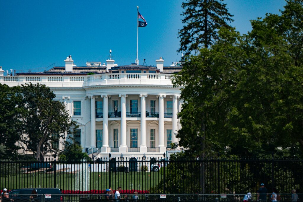 The U.S. White House behind a black fence and under a blue sky, in Washington, D.C.

